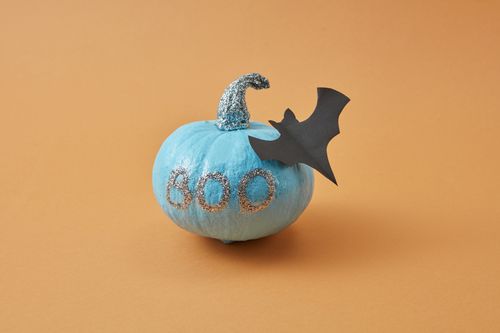 Free Creative Halloween decoration featuring a glittery blue pumpkin with 'Boo' text and paper bat cutout. Stock Photo