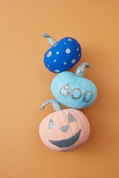 Free A vertical shot of three glittery, painted pumpkins on an orange background for Halloween. Stock Photo