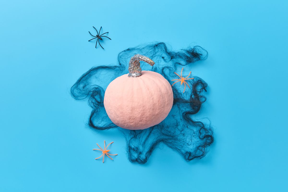 A pink pumpkin with spiders and cobweb effect on a vibrant blue background. Stock Photo.