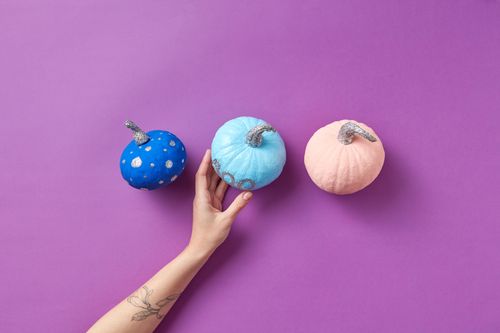 Free High angle view of decorated colorful pumpkins on a purple background with a hand holding one. Stock Photo