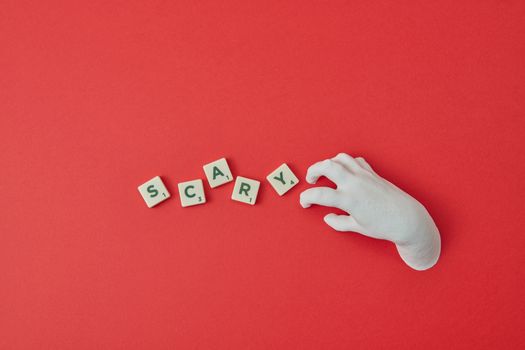 A white hand and Scrabble tiles spelling 'SCARY' on a red background, perfect for Halloween themes.