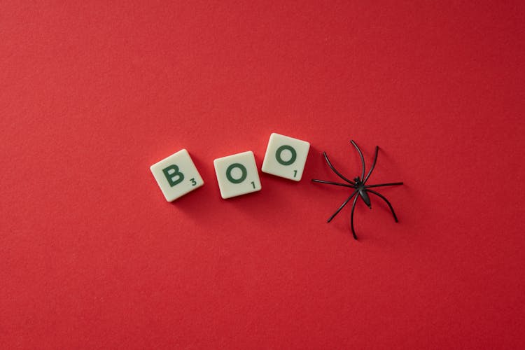 Plastic Scrabble Letters And Plastic Spider On Red Background