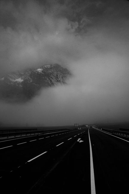 Misty highway in Altenmarkt im Pongau with a dramatic mountain backdrop, captured in monochrome.