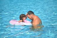 A tender moment between father and daughter in a sunny swimming pool.