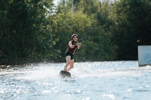 Free A female wakeboarder skillfully navigating water surrounded by lush greenery. Stock Photo