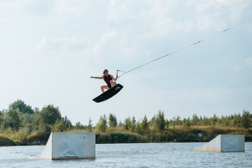 Free A thrilling image of a woman wakeboarding over a water ramp in a scenic outdoor setting. Stock Photo