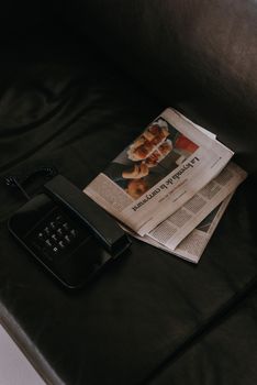 A vintage black telephone and newspaper on a dark leather sofa, conveying a sense of nostalgia.