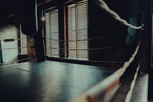 Empty boxing ring in an atmospheric gym with moody lighting and brick walls.