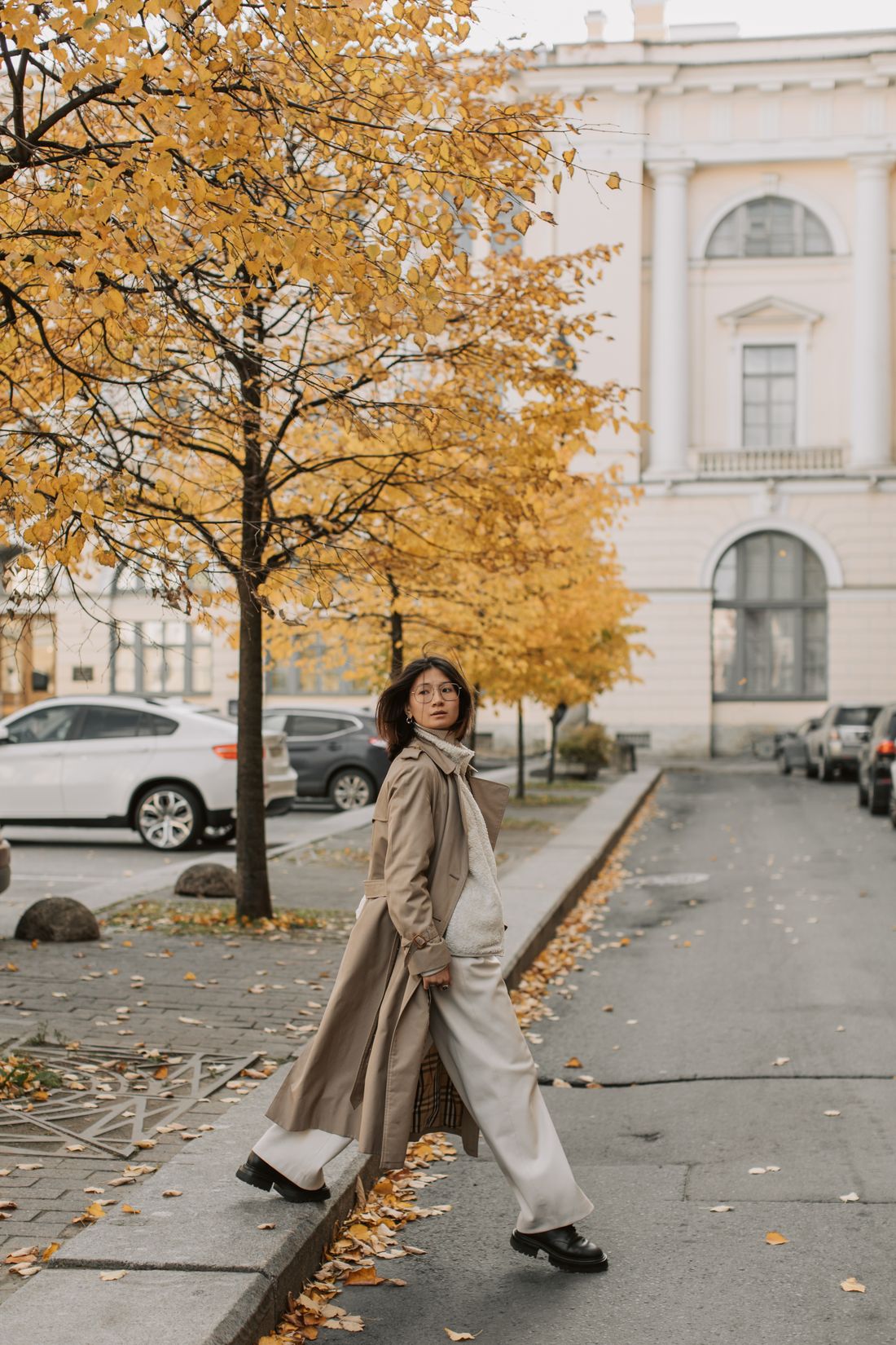Figure in a long coat crossing a tree-lined street in autumn