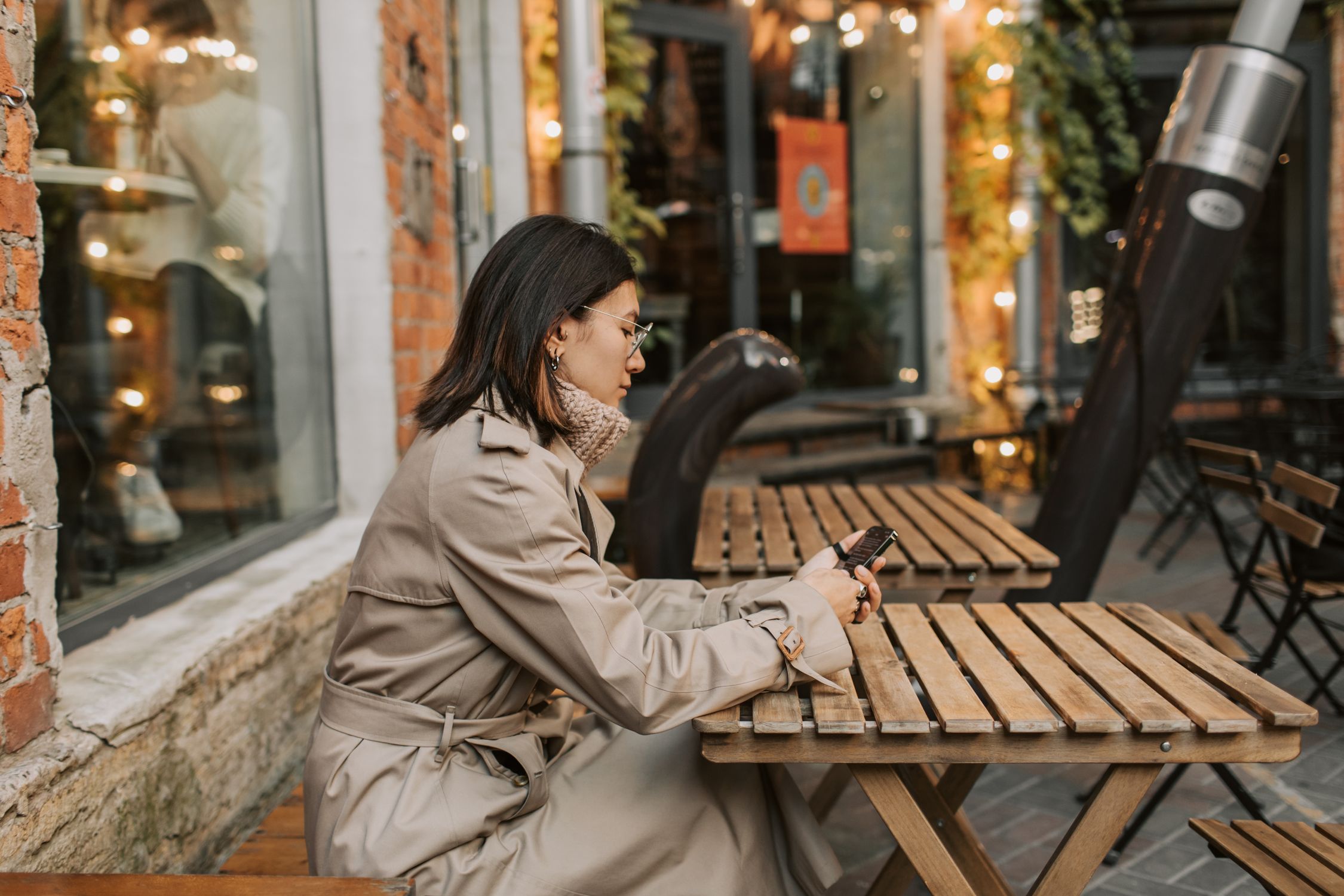 Woman looking at smartphone screen with coffee on table in public setting Woman looking at smartphone screen with coffee on table in public setting