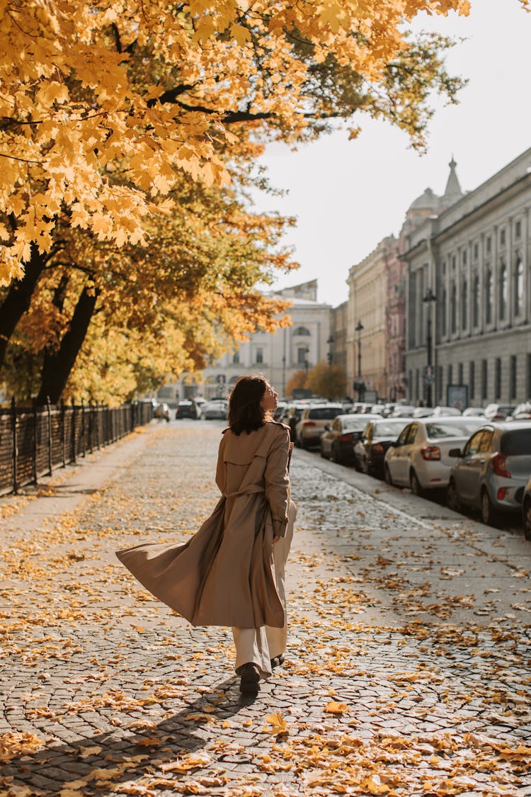 A Woman Wearing A Trench Coat Walking On A Sidewalk