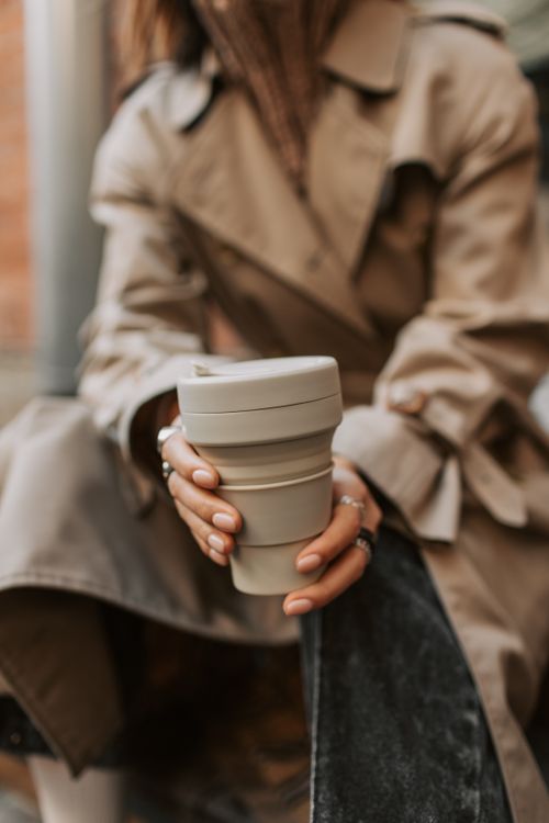 Free A woman in a trench coat holding a collapsible coffee cup outdoors. Stock Photo