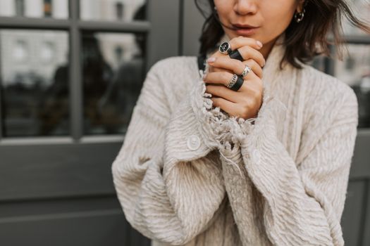 Close-up of a woman clasping hands adorned with rings and a beige coat.