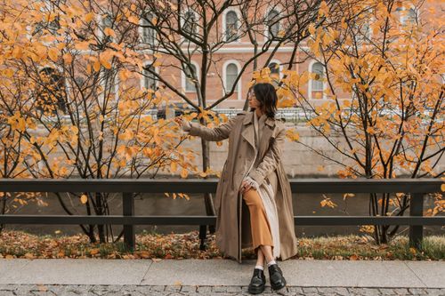 Free Asian woman enjoying fall foliage while sitting on a bench wearing a trench coat. Stock Photo
