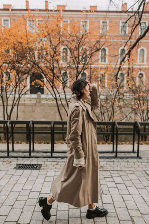 Free Stylish woman in trench coat walking on urban street during autumn. Stock Photo