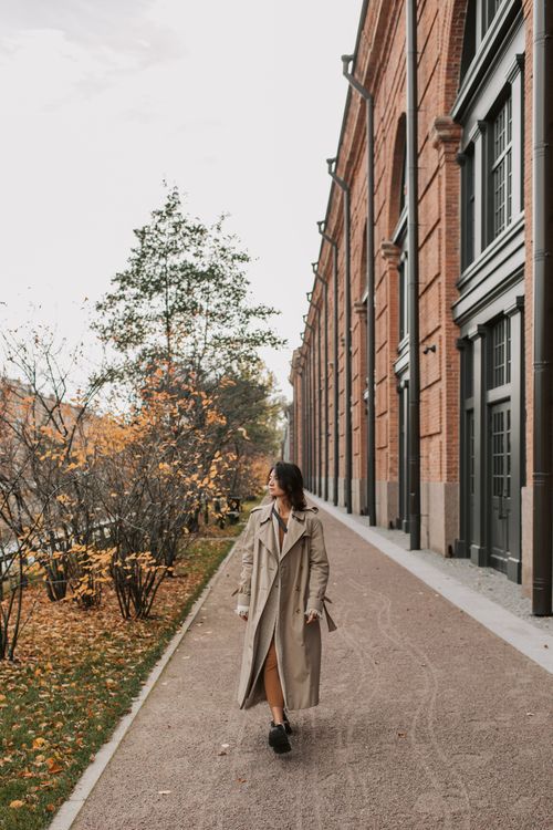 Free Woman in a trench coat walking along a tree-lined city street amidst autumn foliage. Stock Photo