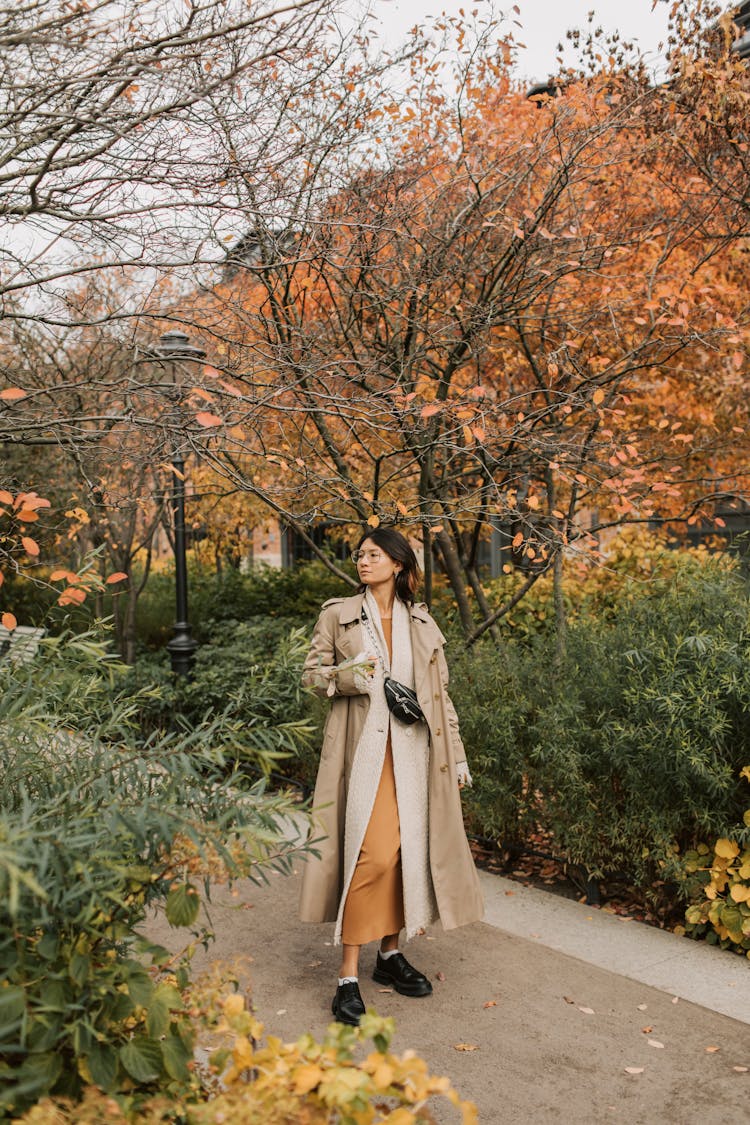 Woman In Brown Trench Coat Standing Near Bare Trees