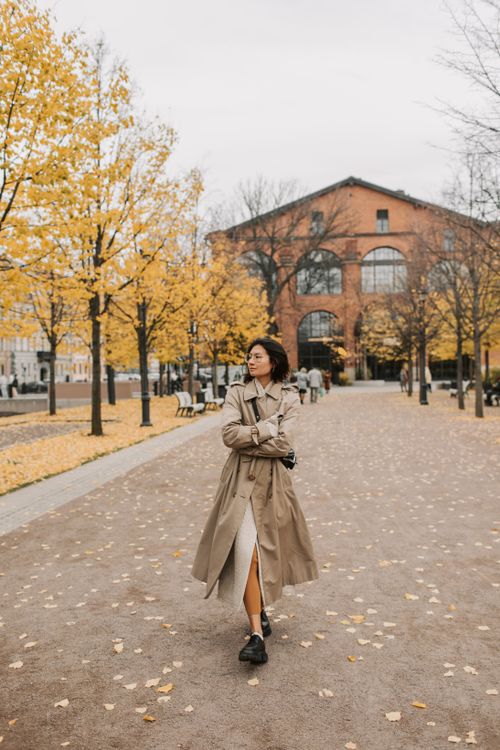 Free Woman in trench coat strolling through a picturesque autumn park with yellow leaves. Stock Photo