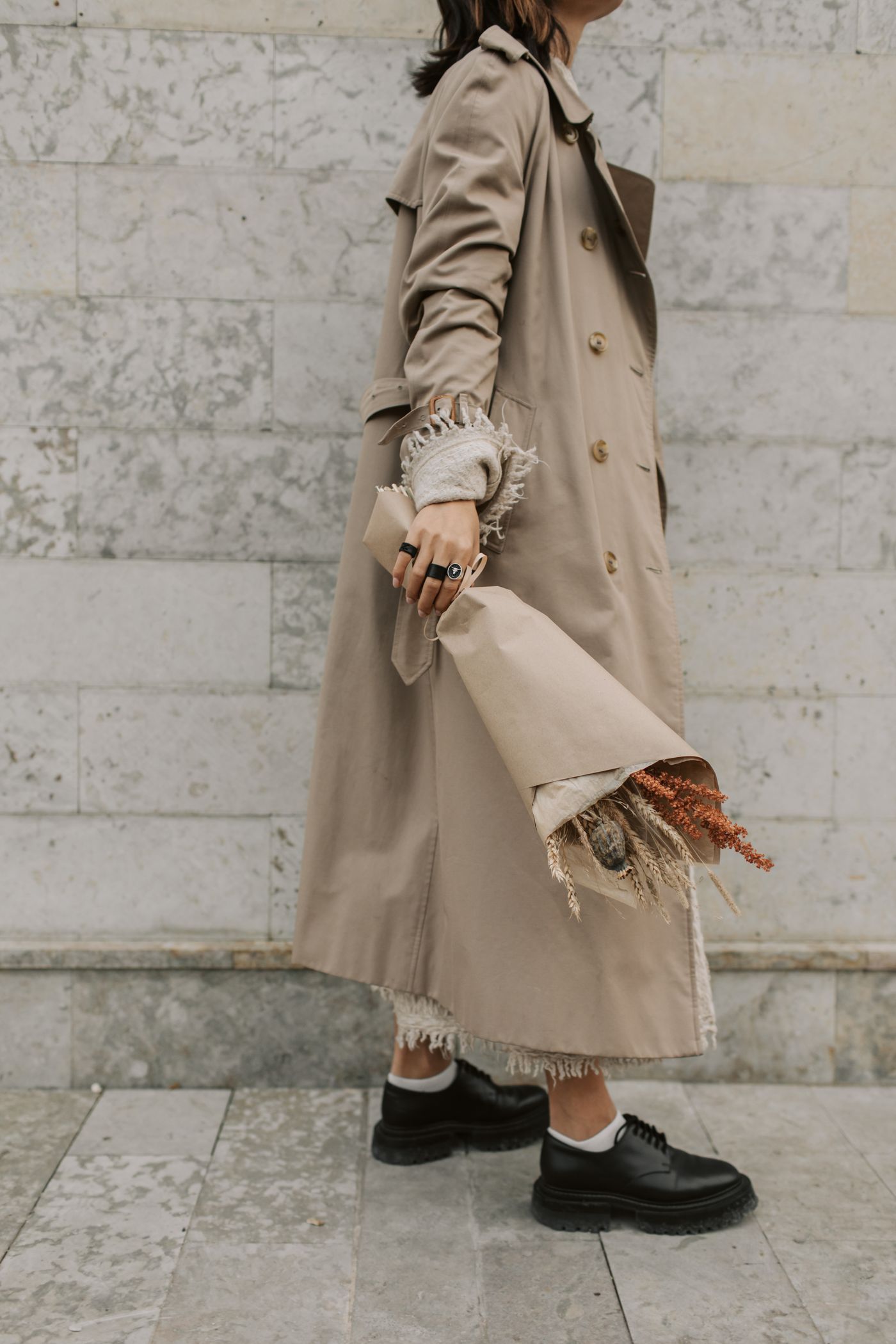 Belted trench coat detail against a pale stone wall