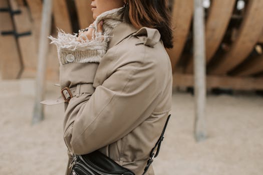 Fashionable woman in a beige coat, side view, outdoors with a sling bag.