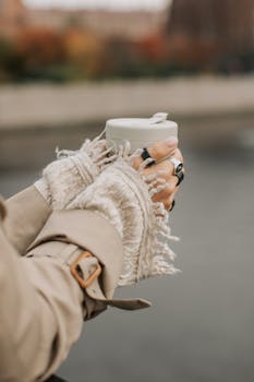 Hands in cozy gloves holding a hot coffee cup outdoors during chilly autumn weather.
