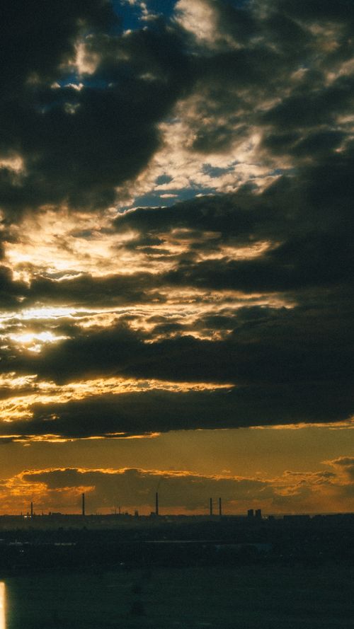 Free A dramatic skyline with dense clouds and a warm sunset glow over an industrial landscape. Stock Photo