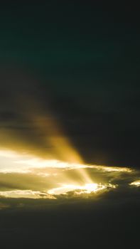 Dramatic sun rays pierce through dark clouds, creating a stunning contrast in the sky.