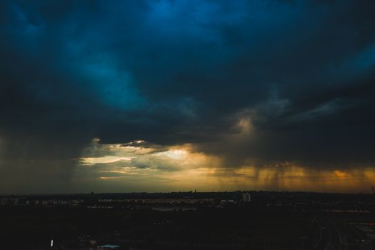 Aerial view of a cityscape under dramatic dark clouds during a colorful sunset, capturing nature's awe-inspiring beauty.