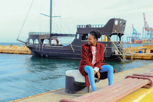 Woman in Red Cardigan Sitting on Black Metal Near Boats