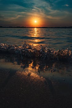 Vibrant sunset over the ocean with waves crashing on the sandy shore.