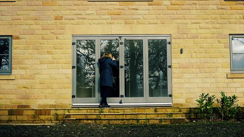 Free A woman in a coat stands on stairs peering into a glass door of a brick house. Stock Photo