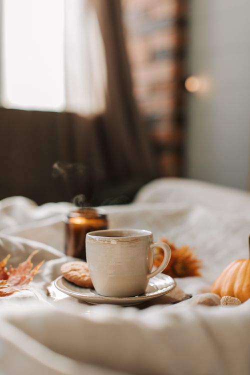 Free Warm autumn scene with a steaming cup of coffee, cookies, and seasonal decor on a bed. Stock Photo