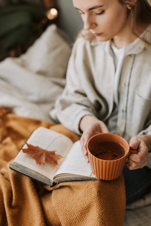 Free Woman Reading a Book while Drinking a Cup of Tea Stock Photo
