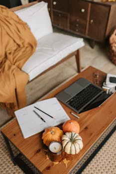 Inviting autumn-themed workspace with pumpkins, notebook, and laptop on a wooden table indoors.