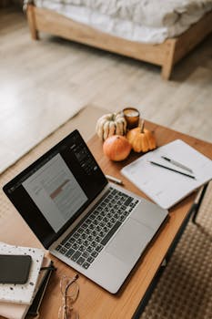 Warm and inviting home workspace featuring a laptop, pumpkins, and cozy fall decor on a wooden desk.