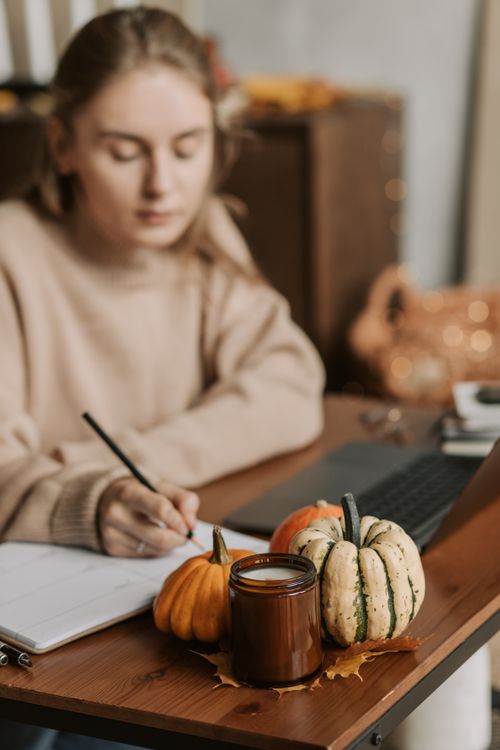 Free A woman writing in a notebook in a home workspace with pumpkins and a candle for a warm autumn vibe. Stock Photo