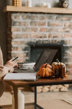 A warm, inviting home office scene featuring a laptop surrounded by autumn decor and a brick fireplace backdrop.
