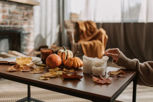 Warm autumn scene with candles, pumpkins, and leaves on a wooden table indoors.