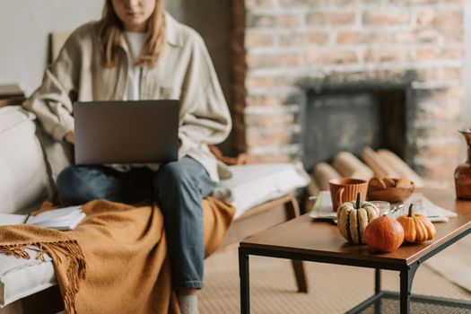 Woman working on laptop in cozy living room with autumn decor and coffee table.