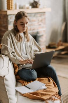Woman working remotely on a laptop at home, sitting on a cozy sofa with a planner.