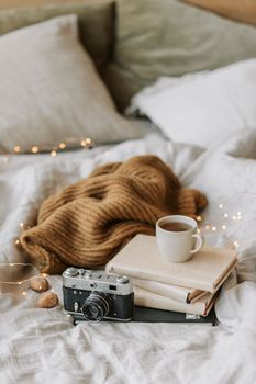 A cozy bedroom setup featuring a vintage camera, stack of books, and a warm blanket for a relaxed ambiance.