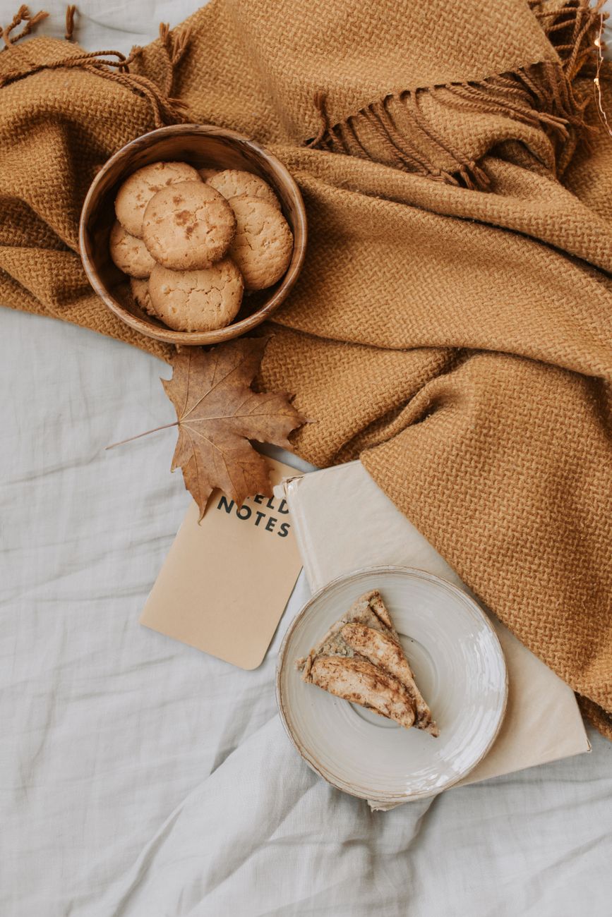 Cozy autumn flat lay with cookies, pastries, and a maple leaf on a warm blanket.