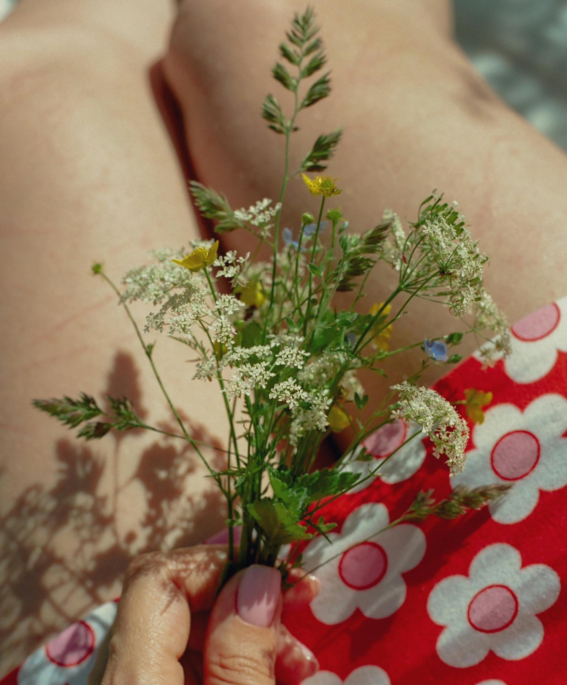 A hand holds a bouquet of wildflowers against floral fabric in sunlight.