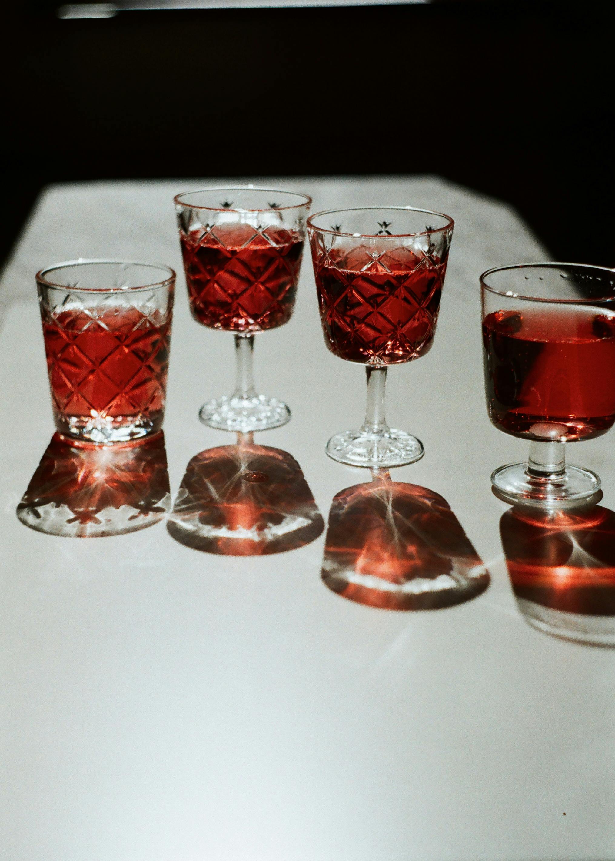 Four elegant red drinks served in crystal glasses casting shadows on a table.