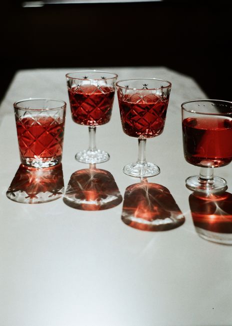 Four elegant red drinks served in crystal glasses casting shadows on a table.