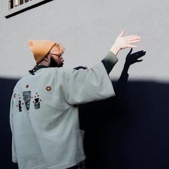 A man wearing a beanie casts a shadow on a wall, creating artistic hand gestures.