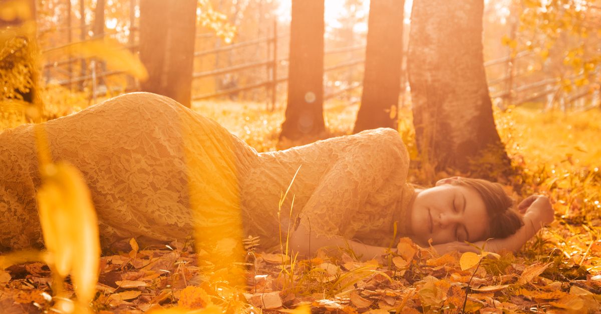A woman peacefully lying on autumn leaves in a forest, basking in golden sunlight.