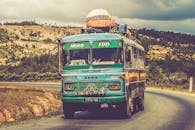 一辆五颜六色的老式巴士在多云的天空下，沿着风景秀丽的乡村道路行驶