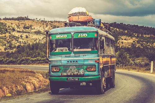 Free Colorful vintage bus traveling on a scenic countryside road under a cloudy sky. Stock Photo