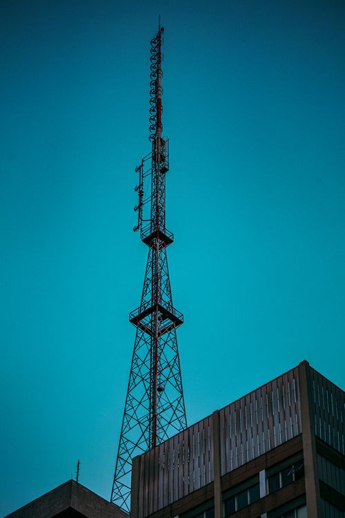 Free A tall telecommunication tower stands against a clear blue sky over urban buildings. Stock Photo